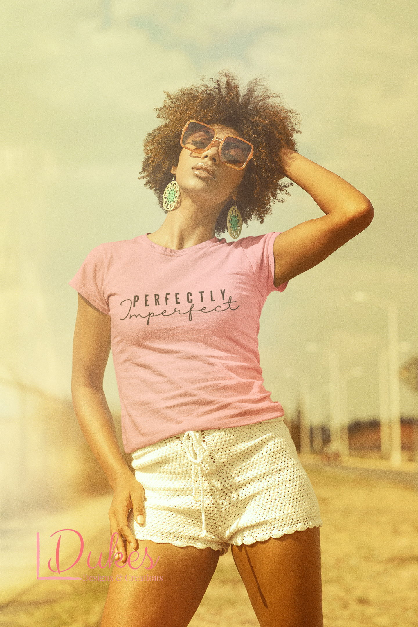 A person wearing a pink t-shirt with the text 'PERFECTLY IMPERFECT' on the front, sunglasses, and a casual pose.