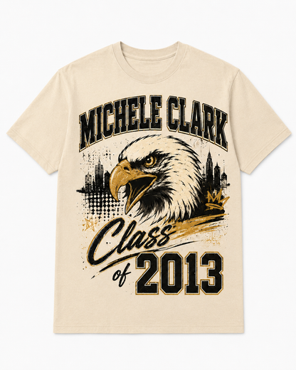 A cream-colored short-sleeve t-shirt with a graphic print featuring an eagle head, the text 'MICHELE CLARK' and 'Class of 2013' in black and gold, set against a plain white background.