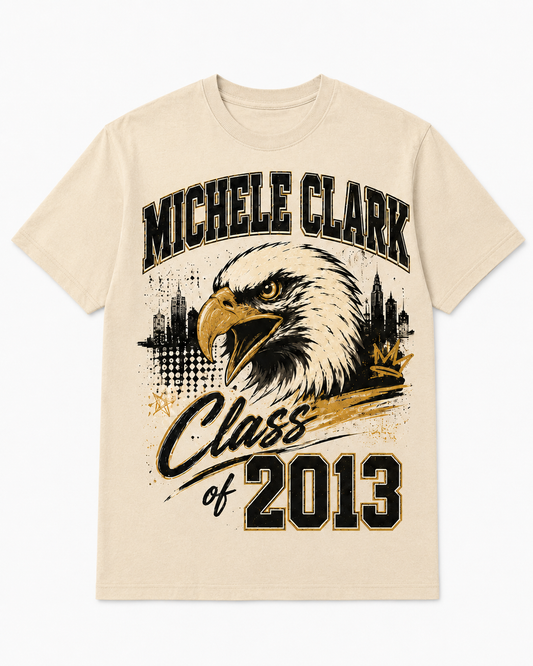 A cream-colored short-sleeve t-shirt with a graphic print featuring an eagle head, the text 'MICHELE CLARK' and 'Class of 2013' in black and gold, set against a plain white background.